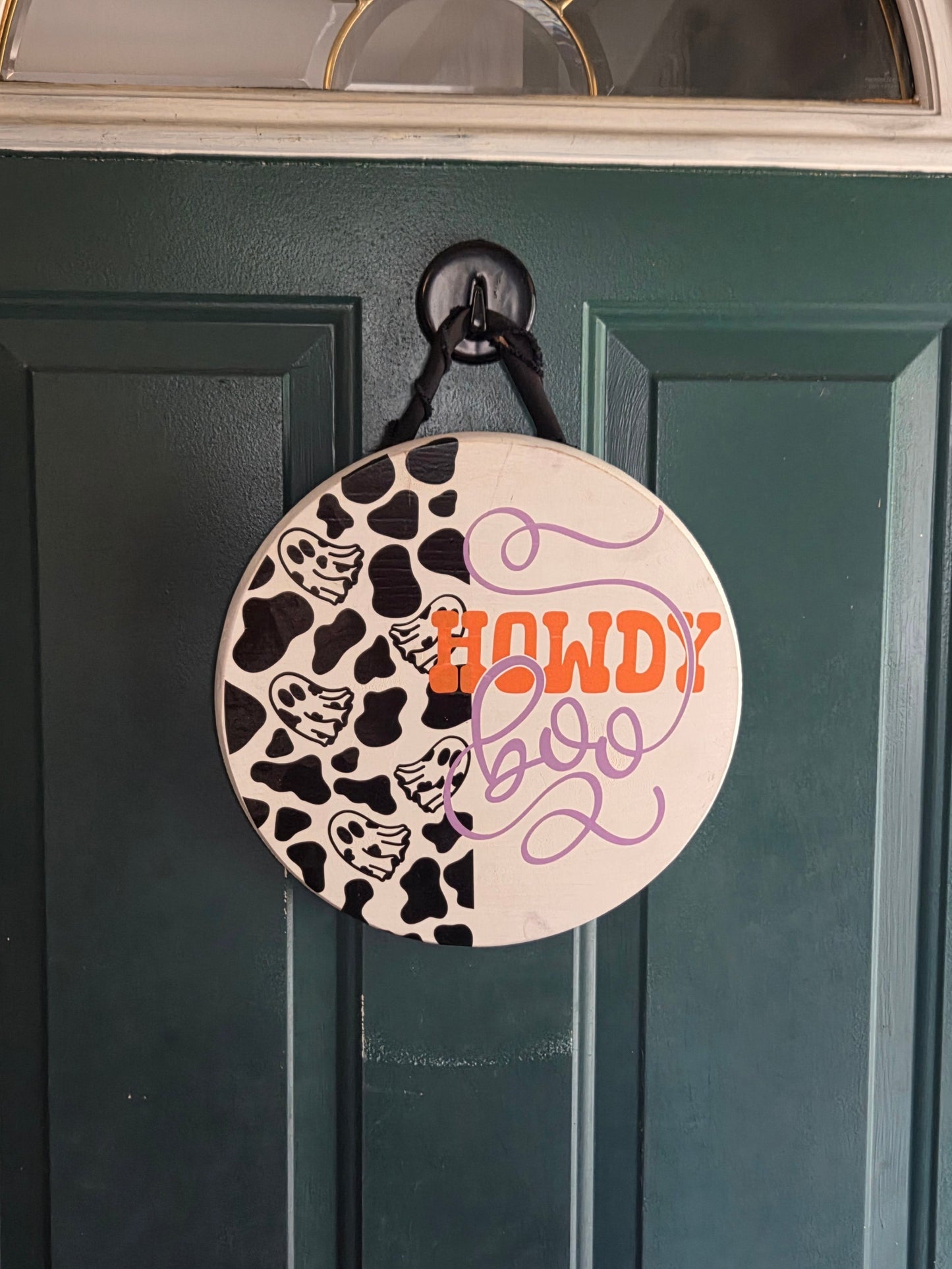 Circular decorative item with cow print and text on a green door - Howdy Boo