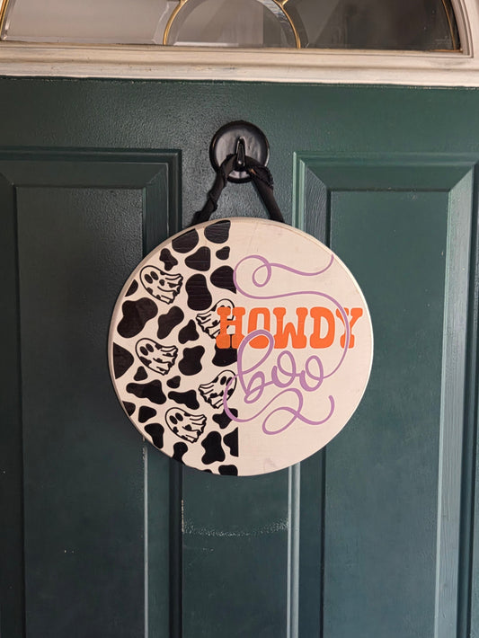 Circular decorative item with cow print and text on a green door - Howdy Boo